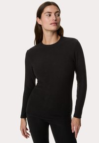 Maglietta nera a maniche lunghe in tessuto morbido, con scollatura rotonda e design aderente, indossata su pantaloni neri. Nessun motivo o dettaglio visibile.