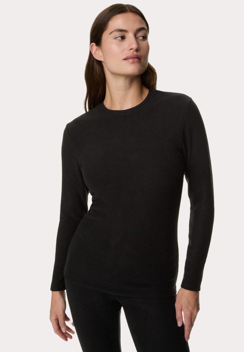 Maglietta nera a maniche lunghe in tessuto morbido, con scollatura rotonda e design aderente, indossata su pantaloni neri. Nessun motivo o dettaglio visibile.