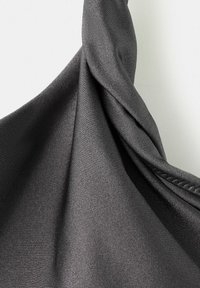 Ciemnoszara tkanina o delikatnej prążkowanej fakturze, skręcona na gładkim jasnym tle, ukazująca fałdy i subtelny połysk.