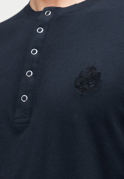 Σκούρο μπλε μπλουζάκι Henley από μαλακό βαμβάκι με στρογγυλή λαιμόκοψη, τρία μεταλλικά κουμπιά και κεντημένο λογότυπο στο στήθος.