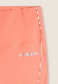 Pantalones cortos deportivos color durazno con textura suave, que presentan ribete blanco y un logo plateado impreso "FREDDY" en el lado inferior.