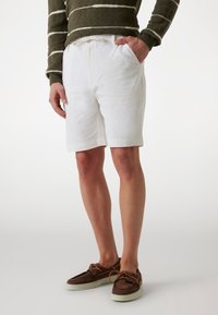 White linen shorts with a relaxed fit, featuring side pockets and a drawstring waist. Paired with brown boat shoes.