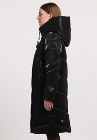 Sort pufferjakke med høj krave og justerbar hætte. Har quiltede sektioner, lynlåslommer og branding på ærmet.