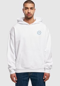 Hvid hættebluse med en forlommes, oversized design, der har et blåt blomsterlogo på venstre bryst og ribbede manchetter og kant.