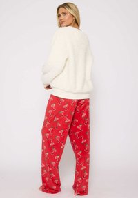 Vit fluffig tröja med långa ärmar, kombinerad med röda pyjamasbyxor som har ett upprepat mönster av cocktailglas. Mjuk textur, lös passform.