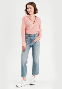 Chemise à rayures rouges et blanches à manches longues, associée à un jean taille haute bleu clair et des baskets blanches.