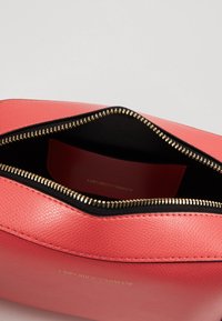 Korale torba skórzana o teksturowanym wykończeniu, czarne wnętrze i złoty zamek błyskawiczny. Posiada logo po wewnętrznej stronie.