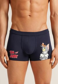 Boxer shorts de color azul marino hechos de una tela elástica, con un gráfico de Tom y Jerry, costuras visibles y un ajuste contorneado.