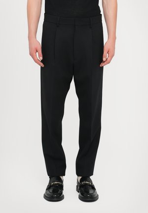 Black tailored trousers with front pleats, straight legs, smooth fabric, and subtle waistband detailing, paired with polished black loafers.
