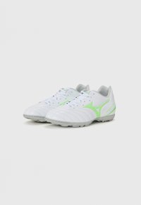 Botas de fútbol blancas con acentos verdes, que cuentan con una parte superior sintética lisa, cordones y una suela texturizada para agarre en superficies de césped.