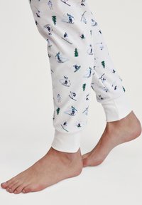 Witte pyjamabroek met een ski-patroon in groen, blauw en roze. Boorden in witte stof; het materiaal lijkt zacht met een gladde textuur.