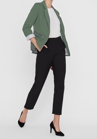 Zelený přizpůsobený blazer s vyhrnutými rukávy, bílý tričko a černé slim-fit kalhoty. Černé lodičky na vysokém podpatku dotvářejí outfit.