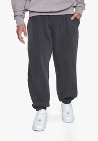 Grå fleece joggerbukser med elastiske mansjetter, med en løs pasform og sidelommer, sammen med hvide sneakers.
