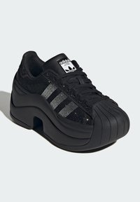 Black athletic shoe featuring a textured fabric upper with black and silver accents, a rounded toe, and a thick rubber sole.