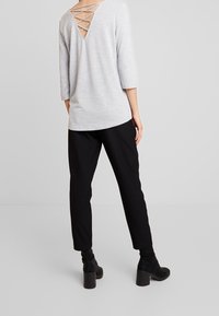 Grå topp med trekvartsärmar och V-formad baksida med korslagda detaljer, kombinerad med svarta smala byxor och ankelskor.