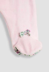 Salopetă roz din fleece cu un mansetă cu model floral și un accent subțire sub formă de fundiță. Textură moale, design confortabil și formă rotundă a vârfului.