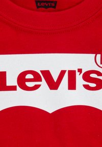 Rotes Baumwoll-T-Shirt mit einem weißen Logo, das den Text "Levi's" zeigt. Der Halsausschnitt ist gerippt und die Nähte sind entlang der Kanten sichtbar.