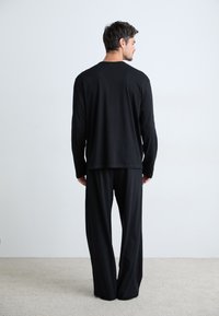 Haut noir à manches longues et pantalon ample en tissu doux. La tenue présente un design simple avec une silhouette décontractée.
