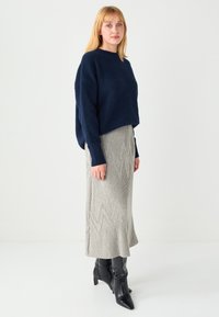 Marineblauer Strickpullover mit lockerem Sitz und gerippten Bündchen, kombiniert mit einem grauen, gerippten Rock mit Zickzackmuster und schwarzen Stiefeletten.