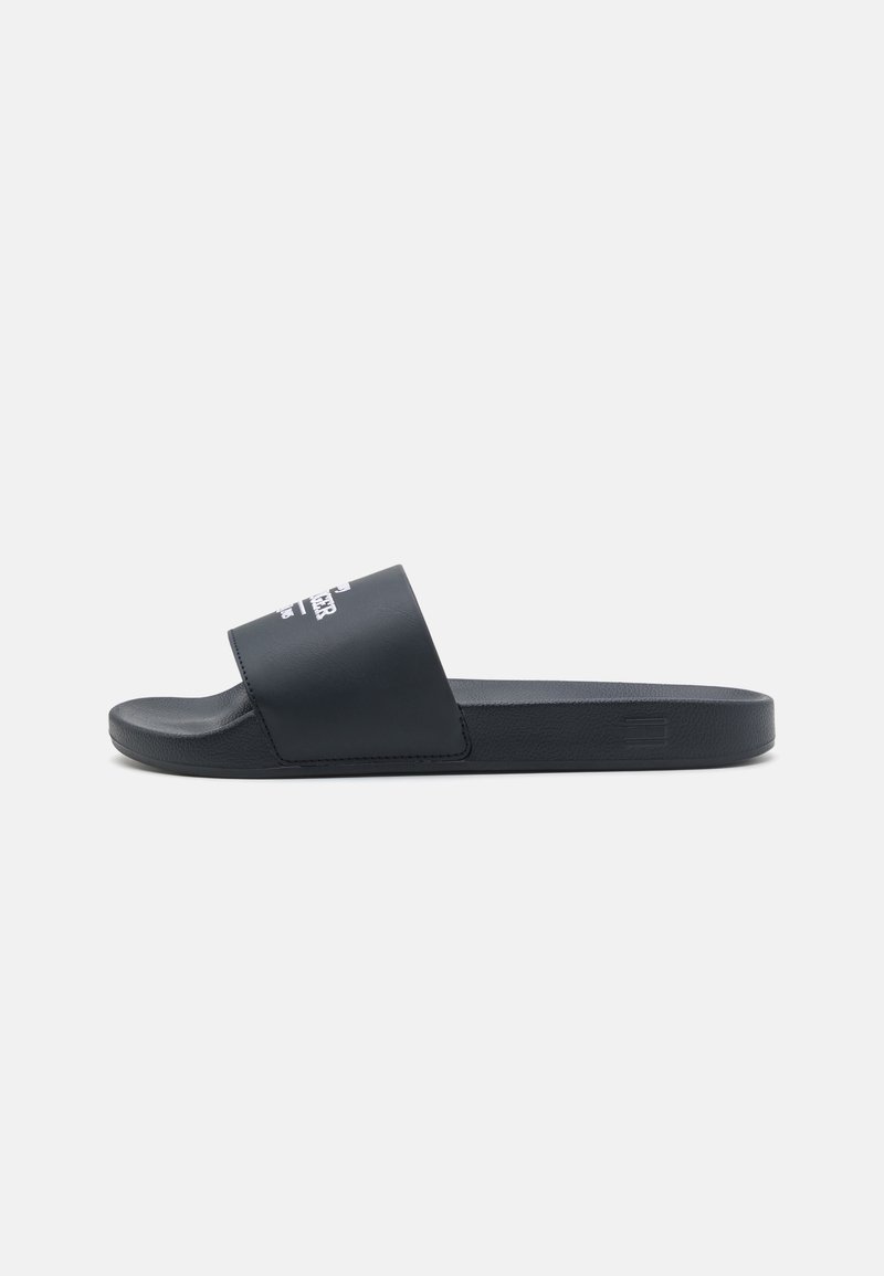 Black slide sandal with a smooth, matte rubber upper and textured footbed. Features a minimalist design with printed branding on the strap.