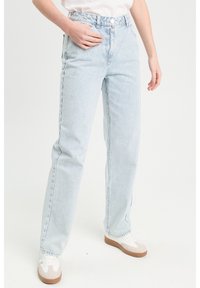 Jean à rayures bleu clair avec une coupe décontractée, fabriqué en tissu en denim. Doté d'une fermeture à bouton et de quatre poches. Associé à des baskets blanches.