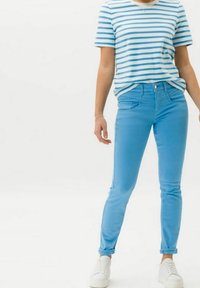 Panjang jins biru dengan tekstur halus, dilengkapi dengan loop sabuk dan saku depan. Dipadukan dengan kemeja lengan pendek bergaris biru dan putih.