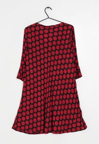 Rot- und schwarzgepunktetes Kleid aus glattem Stoff. Mit Dreiviertelärmeln und einer lockeren A-Linien-Silhouette. Hängt an einem schwarzen Haken.