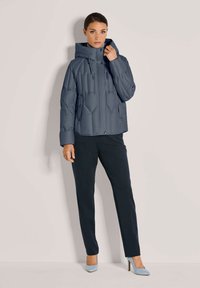 Grijze gewatteerde jas met een capuchon, voorzien van een ritssluiting aan de voorkant, drukknoopsluiting en een gestikt ontwerp. Gekocht met donkere broeken en lichtblauwe hakken.