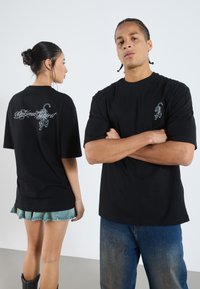 T-shirts noirs surdimensionnés avec un graphisme de tigre et du texte au dos ; un t-shirt présente un petit design de tigre sur le devant, avec des manches courtes.