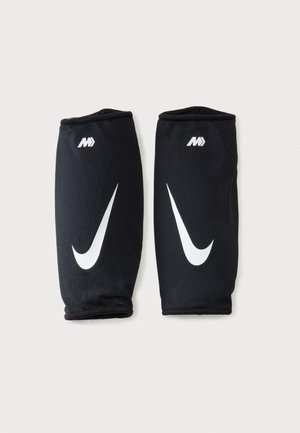 Pár čiernych návlekov Nike na lýtka s bielym logom Swoosh a iniciálami "MV" na neutrálnom pozadí.