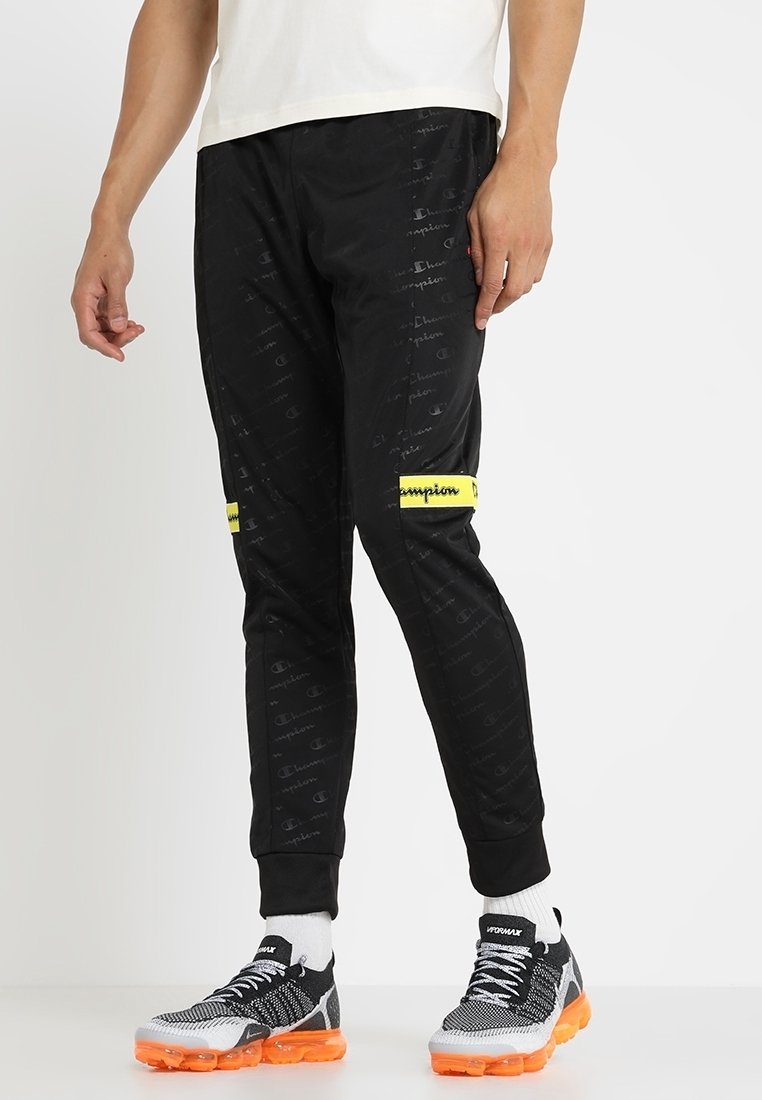 Svarta joggers med ett subtilt mönster med gula accenter, en smal passform och elastisk midja. Bärs med svarta och orange sneakers.