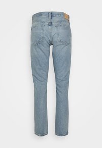 Jasnoniebieskie dżinsy z prostymi nogawkami, z wysokim stanem, pięcioma kieszeniami oraz brązową skórzaną naszywką z tyłu.