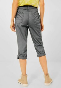 Pantalons gris coupés avec une texture lisse, dotés de poignets retournés, de poches arrière et d'une taille ajustée, associés à des baskets beige clair.