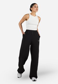 White ribbed tank top paired with loose black sweatpants featuring an elastic waistband and side pockets, set against a plain background.