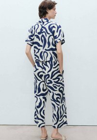 Lightweight, patterned two-piece outfit featuring a loose short-sleeve shirt and high-waisted pants in navy and cream with abstract curves.