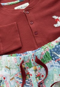 Sarkans kokvilnas viļņotais tops ar trim pogām un polāro lāci uzšuvēm, apvienots ar elastīgu jostasvietas pidžamu apakšbiksēm, kas rotātas ar daudzkrāsu dzīvnieku rakstu.