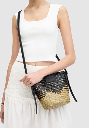 Sac seau en tissu tissé avec un motif dégradé noir et beige, équipé d'une bandoulière en cuir noir et d'un patch logo rectangulaire à l'avant.