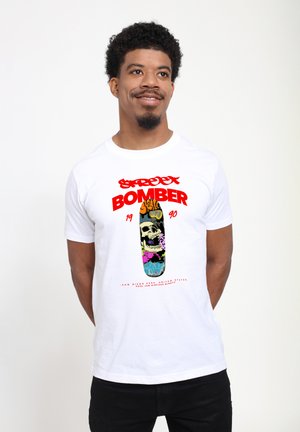White cotton t-shirt featuring bold red text "STREET BOMBER 1990" above a colorful skateboard graphic with a skull and various patterns.