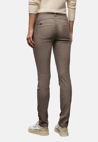 Pantaloni marroni attillati con tasche posteriori, dettagli di cucitura sottili e un tessuto leggero e liscio. Indossati con sneakers di colore chiaro.