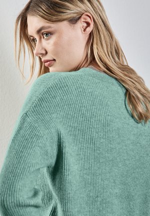 Mintgrüner Strickpullover mit geripptem Muster, weitem Ausschnitt und überschnittenen Schultern, von der Seite aufgenommen, um eine lockere Passform zu zeigen.