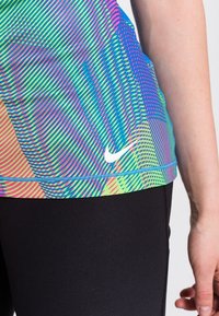 Camiseta atlética de Nike en un vibrante patrón multicolor con rayas horizontales y diagonales. Cuenta con un logo blanco y leggins negros.