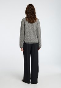 Grau gestreifter Strickpullover mit langen Ärmeln, getragen mit schwarzen weiten Hose. Weiche Textur und lässige Passform.