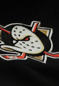 Gesticktes Patch mit einem stilisierten Tiergesicht in roten Akzenten, auf einem schwarzen Stoffhintergrund. Goldene und weiße Details verfeinern das Design.