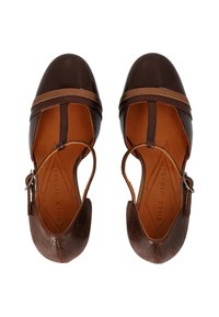 Scarpe in pelle marrone con punta arrotondata, texture dettagliata e cinturino alla caviglia. Presentano cinturini marroni a contrasto e un interno liscio.