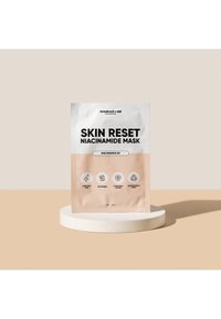 Niacinamid-Maske in einem weißen und pfirsichfarbenen Beutel auf einem runden weißen Sockel. Mit Symbolen, die Vorteile anzeigen: ebenmäßiger Hautton, Macadamia, klärend, biologisch abbaubar.