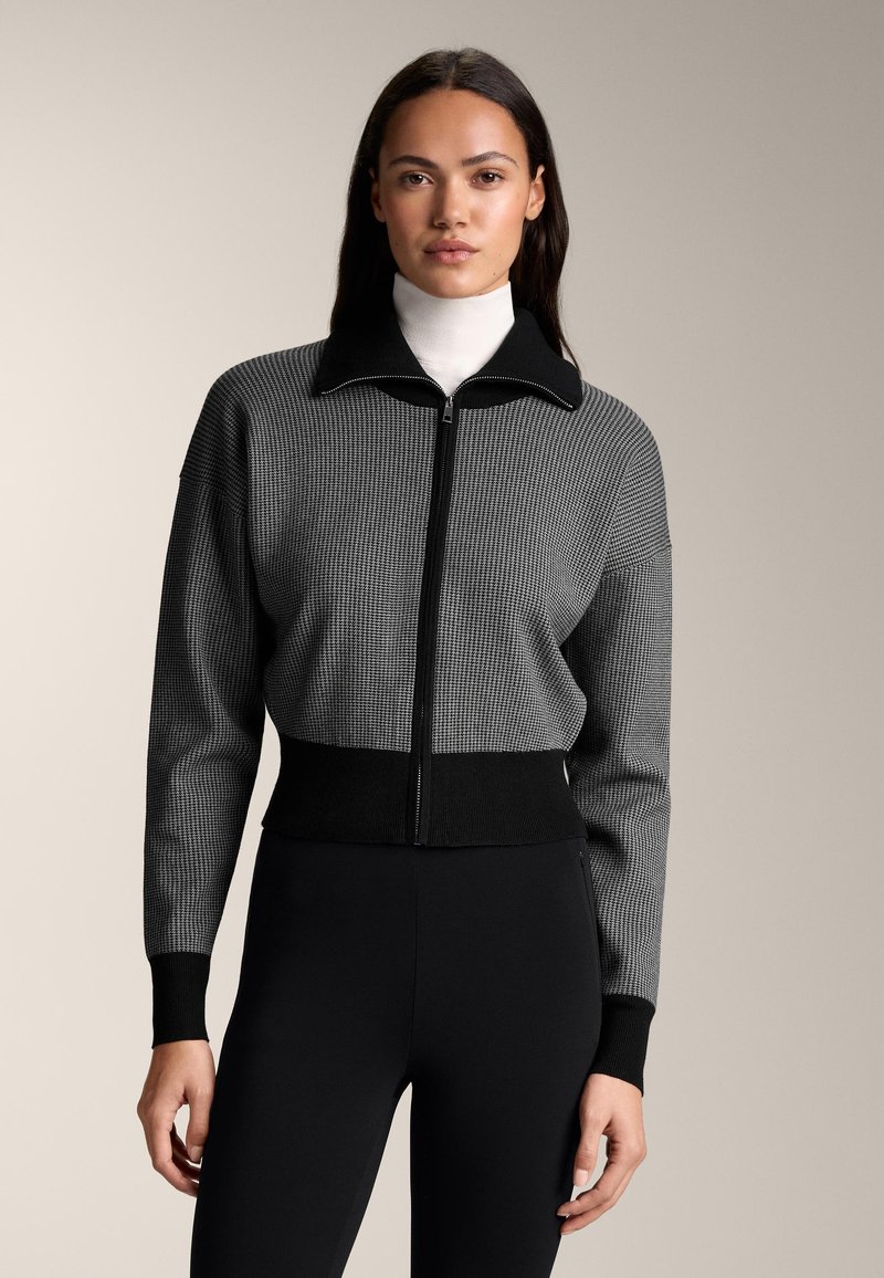 Czarna i szara żebrowana kurtka na zamek z wysokim kołnierzem, dopasowanym pasem i teksturowaną tkaniną, zestawiona z czarnymi legginsami.