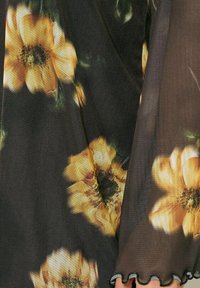 Tessuto trasparente con un grande motivo floreale giallo su uno sfondo scuro, caratterizzato da un orlo scallopato e sottili variazioni di texture.