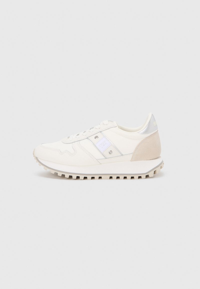 Des baskets athlétiques blanches avec une tige en tissu texturé, des accents argentés et un talon en daim beige. La semelle présente un design rainuré pour une meilleure adhérence.