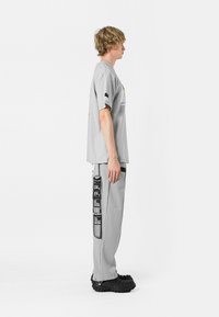Camiseta gris de manga corta y corte holgado; pantalones grises con bolsillos de carga; ambos hechos de tejido suave; calzado negro texturizado.