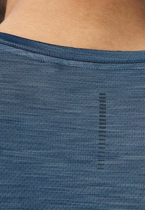 Primer plano de la parte superior de la espalda de una persona que lleva una camiseta deportiva azul texturizada con un logo negro vertical cerca del centro.